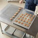 A person wearing a blue apron using a wire rimmed aluminum bun pan to bake cookies.