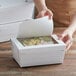 A person opening a Bio-Pak white paper take-out box with a window filled with food.