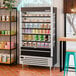 A black and silver open-air curtain merchandiser refrigerator displaying various drinks and food containers.