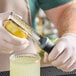 A person in gloves using a Barfly stainless steel zester to peel a lemon.