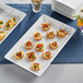 A white marble rectangular melamine platter with appetizers on a table.