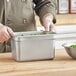 A person using a Choice 1/4 size stainless steel steam table pan to serve food on a wooden counter.