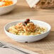 A white round shallow melamine bowl with a 14 oz. capacity, shown holding a serving of food.