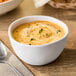 A white melamine bouillon cup filled with creamy soup and garnished with herbs.