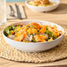 A white round shallow melamine bowl filled with a fresh salad, placed on a woven placemat.