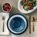 A table setting with a blue plate, American Metalcraft Linen Melamine Bouillon cup, fork, knife and spoon.