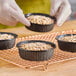 A person holding a tray of Solut black rolled rim baking cups filled with baked goods.