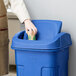 A person in an apron putting a cup into a blue Toter trash can.