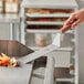 A hand using a Mercer Culinary Praxis square edge turner to cut vegetables on a grill.