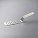 A Dexter-Russell perforated turner with a white plastic handle.