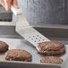 A person using a Dexter-Russell perforated turner to cook a burger.