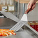 A person using a Mercer Culinary Praxis perforated turner with a rosewood handle to cut vegetables.