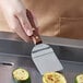 A person using a Dexter-Russell rosewood handled mini turner to cook zucchini.