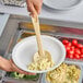 A person using a Cambro beige perforated spoon to serve macaroni and cheese at a salad bar.