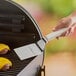 A hand holding a Dexter-Russell square edge hamburger turner over burgers on a grill.