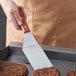A person using a Dexter-Russell hamburger turner to cook burgers on a grill.