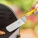A hand holding a yellow Mercer Culinary Millennia turner over a grill.