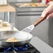 A person using a Mercer Culinary fish turner with a rosewood handle to flip fish in a pan.