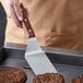 A person holding a Dexter-Russell rosewood hamburger turner over a hamburger patty cooking on a pan.