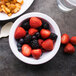 A Carlisle white rimmed nappie bowl filled with fruit on a table with french fries.