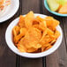 A Carlisle white rimmed nappie bowl filled with potato chips alongside a bowl of fruit.