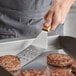 A person using a Vollrath perforated stainless steel hamburger turner to cook burgers on a grill.
