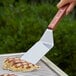 A hand holding a Dexter-Russell Traditional Solid Turner with a rosewood handle over a grill.
