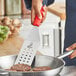 A person using a Mercer Culinary perforated spatula to cook meat patties in a pan.