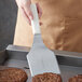 A person using a Dexter-Russell solid hamburger turner to cook burgers on a grill.