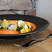 A RAK Porcelain Trinidad cedar and black porcelain plate with food on a table.