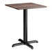 A square standard height table with a textured walnut finish top and a black cross base plate.