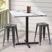 A Lancaster Table & Seating square counter height table with a smooth brown finish and cross base plate with two stools on a patio.