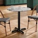 A round standard height table with a smooth Versilla finish and a black cross base plate.