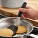A black silicone flexible solid spatula being used to flip pancakes in a frying pan.