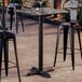 A square bar height table with a smooth, dark stone-like finish and a black cross base plate.