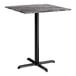 A square bar height table with a smooth dark finish top and a black cross base plate.