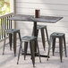 A Lancaster Table & Seating rectangular table with a smooth finish and cross base plate on a porch with black stools.