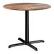 A round standard height table with a textured Yukon oak finish top and a black cross base plate.