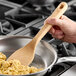 A wooden spatula being used to stir food in a stainless steel pan on a stovetop.