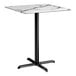 A square bar height table with a smooth white marble-like top and a black cross base plate.