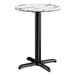 A round table with a smooth white and gray marble-like top and a black metal cross base.