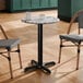 A round standard height table with a smooth Versilla finish and a black cross base plate.