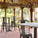 A Lancaster Table & Seating Excalibur bar height table and chairs on a covered patio.