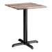 A square standard height table with a textured mixed plank finish top and a black cross base plate.