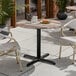A round standard height table with a textured mixed plank finish and a black cross base plate.