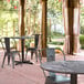 A Lancaster Table & Seating Excalibur round table with a cross base plate on a brick patio with two chairs.