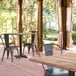 A Lancaster Table & Seating Excalibur table with a textured Yukon Oak finish and cross base plate on a brick patio with chairs.