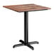 A square standard height table with a textured Yukon oak finish top and a black cross base plate.