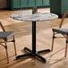 A round standard height table with a smooth Versilla finish and a black cross base plate.