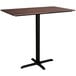 A rectangular bar height table with a textured walnut top on a black cross base.